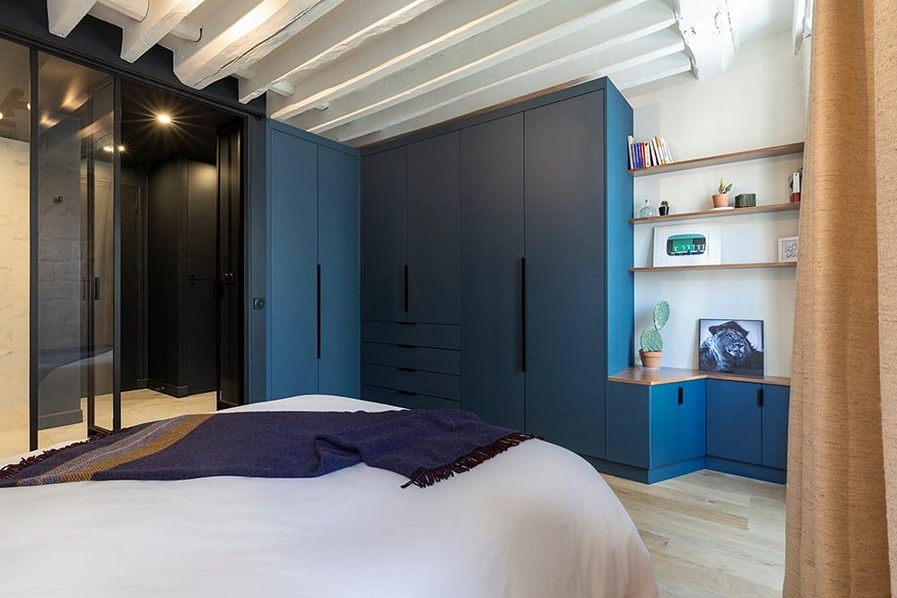 Spacious bedroom with blue cabinetry, shelves, and decorative accents against wooden beams.