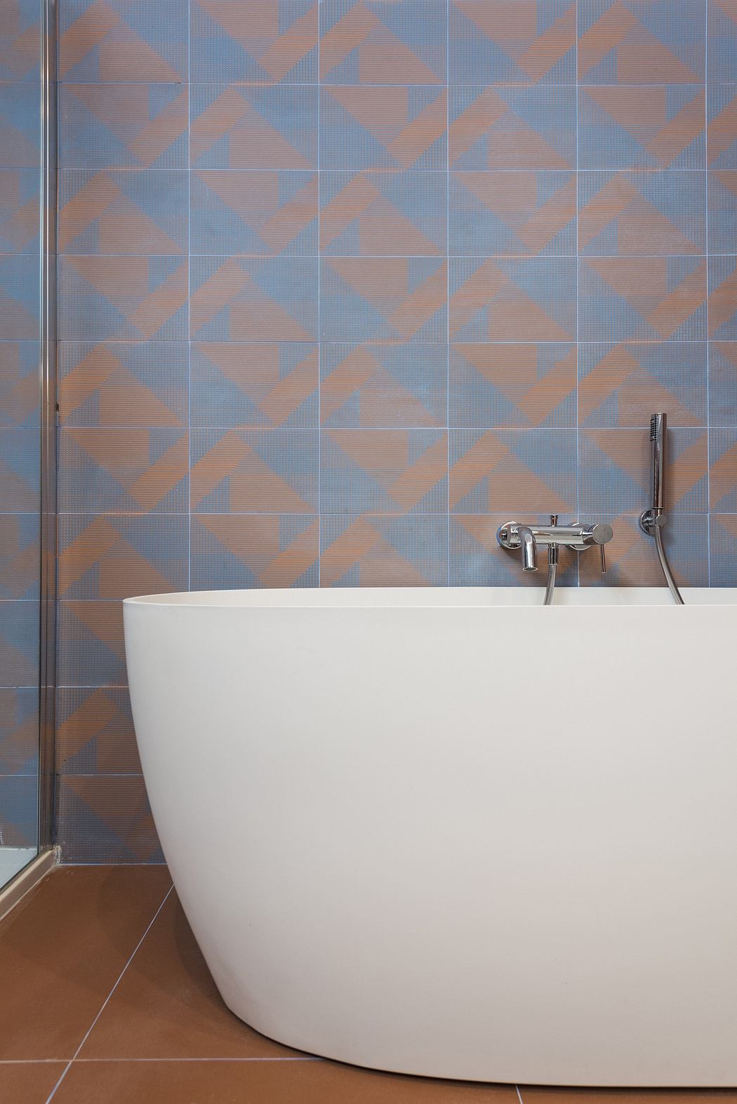 Modern bathroom with geometric tile pattern and freestanding white bathtub.