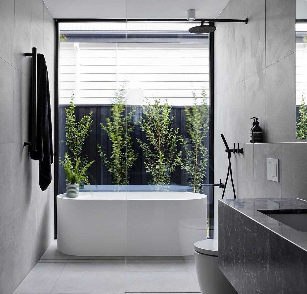A modern bathroom with a freestanding white bathtub, black accents, and lush greenery visible outside.