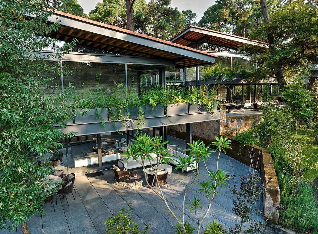 A modern, open-concept glass house surrounded by lush greenery and a tranquil pond.