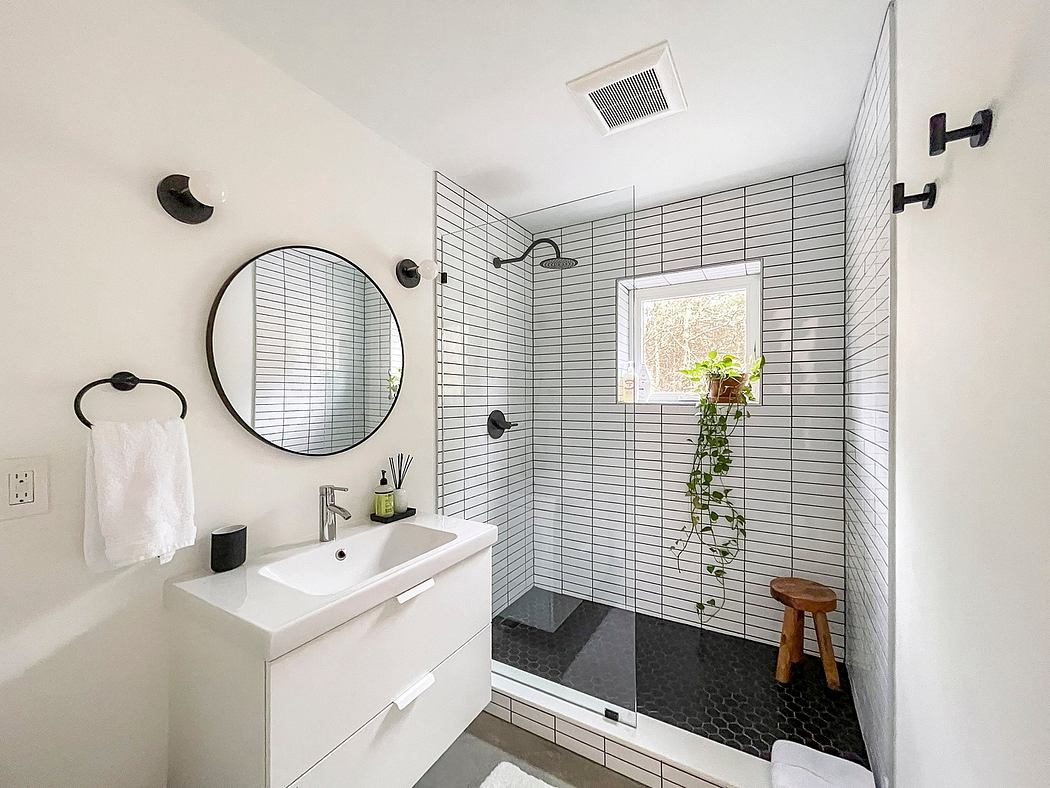 Modern, minimalist bathroom with sleek tiled walls, circular mirror, and potted plant.