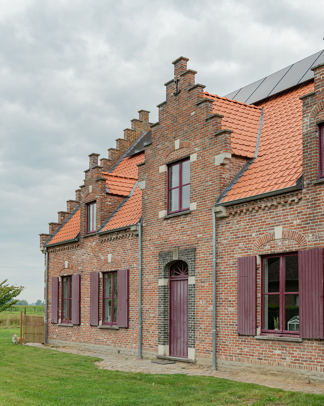 Charming brick farmhouse with ornate facade, terra cotta tiles, and purple shutters.