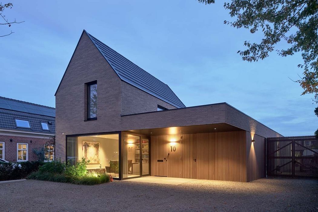 Modern residential building with pitched roof, wooden facade, and illuminated entryway.