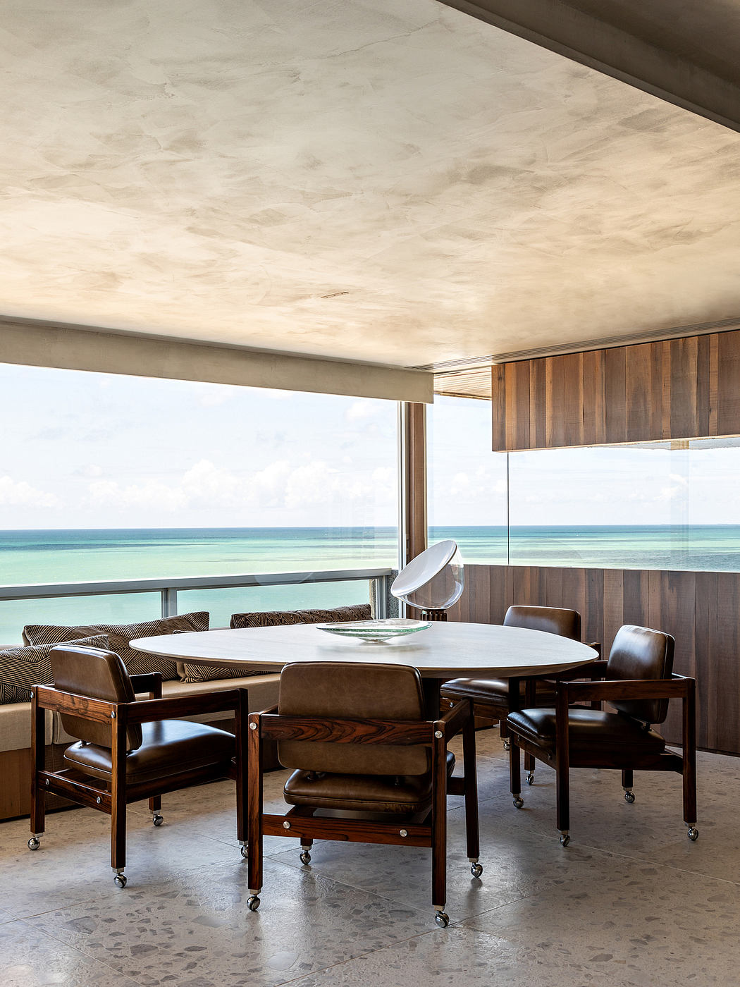 Plush leather chairs around a circular dining table, set against a scenic ocean view.