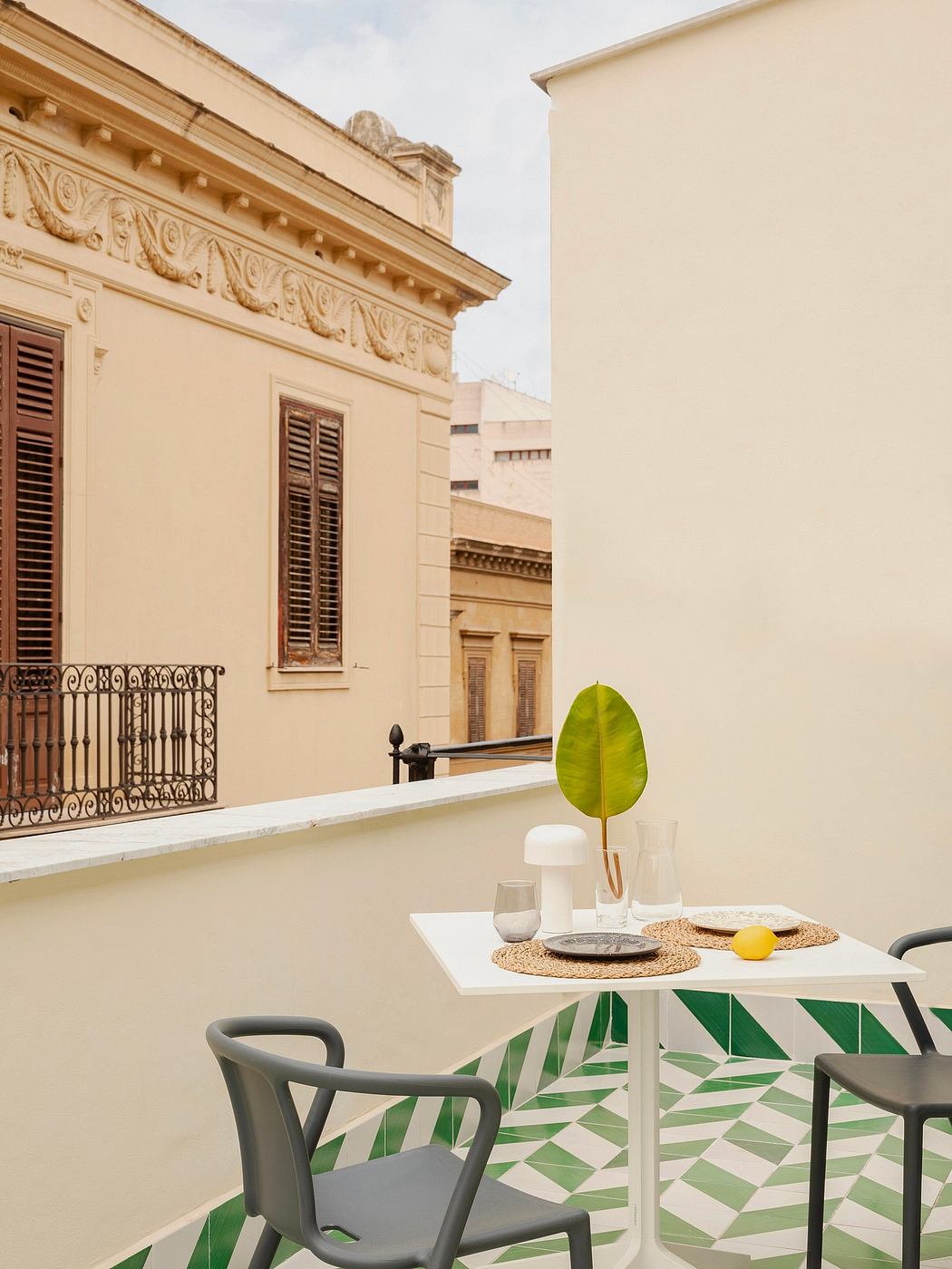 Ornate beige facade, green geometric patio tiles, white modern table setting.