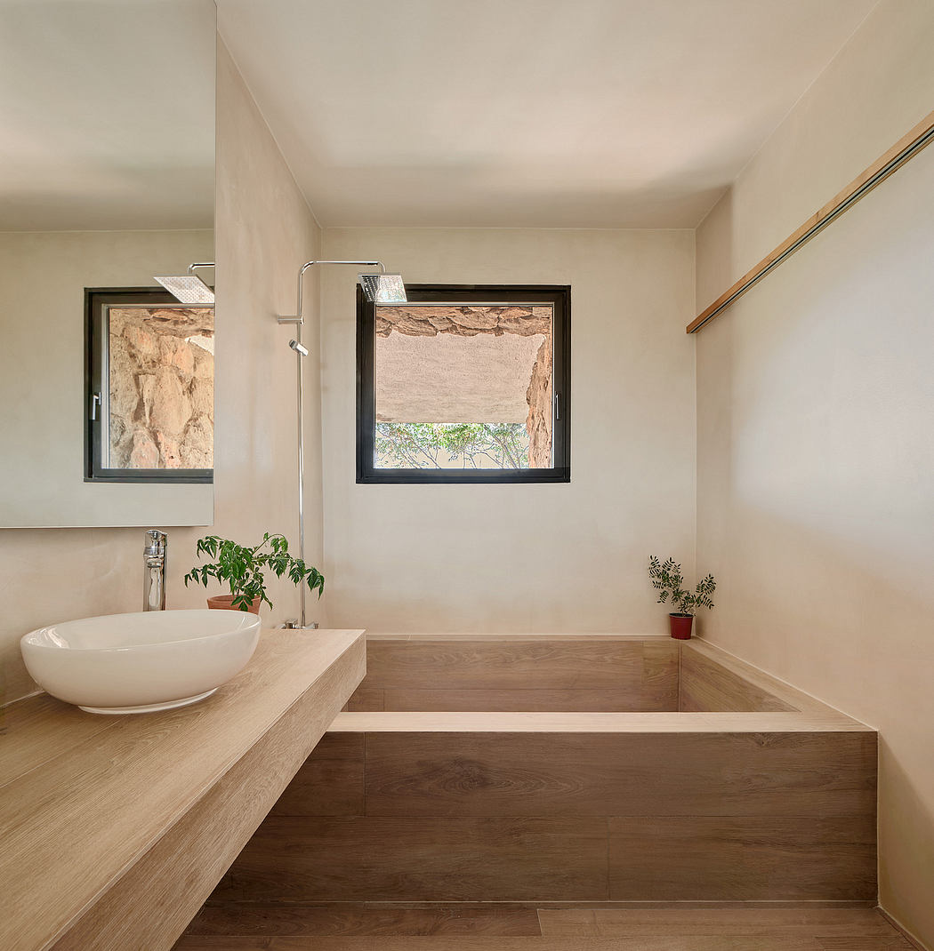 A modern bathroom with a white vessel sink, wooden vanity, and large window overlooking nature.