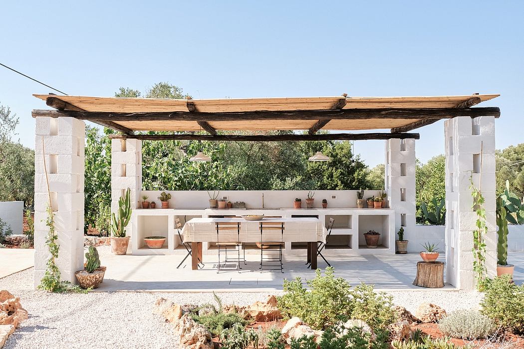 A rustic outdoor kitchen with a wooden pergola, potted plants, and a stone and tile dining area.