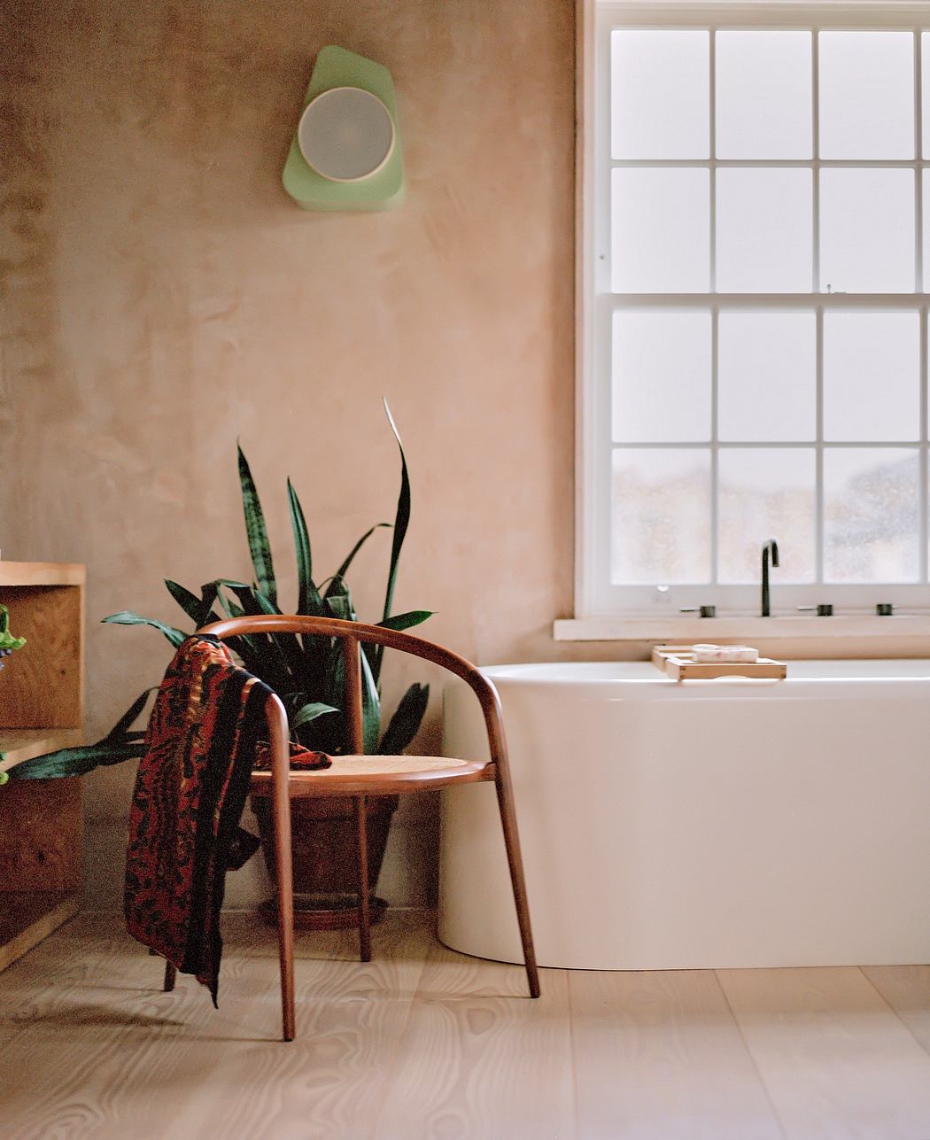 Cozy bathroom with rustic wooden chair, potted plants, and modern white tub.