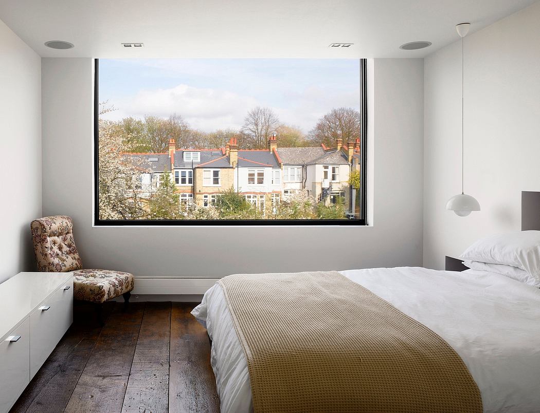 Spacious bedroom with large window overlooking urban skyline and lush foliage.