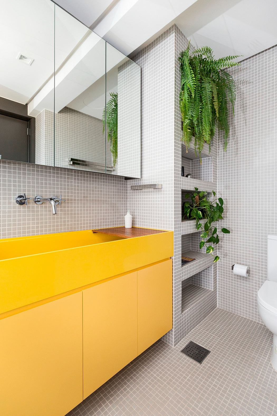 Sleek, modern bathroom featuring a bold yellow vanity, mosaics, and lush greenery.