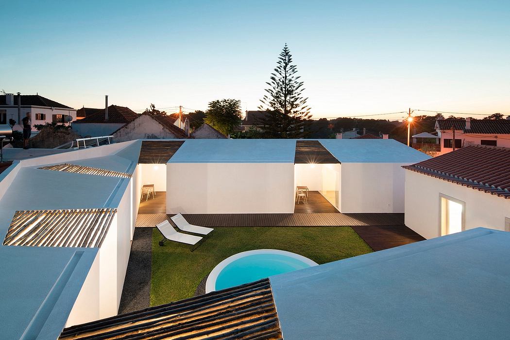 A modern residential complex with clean lines, a pool, and lush greenery at sunset.
