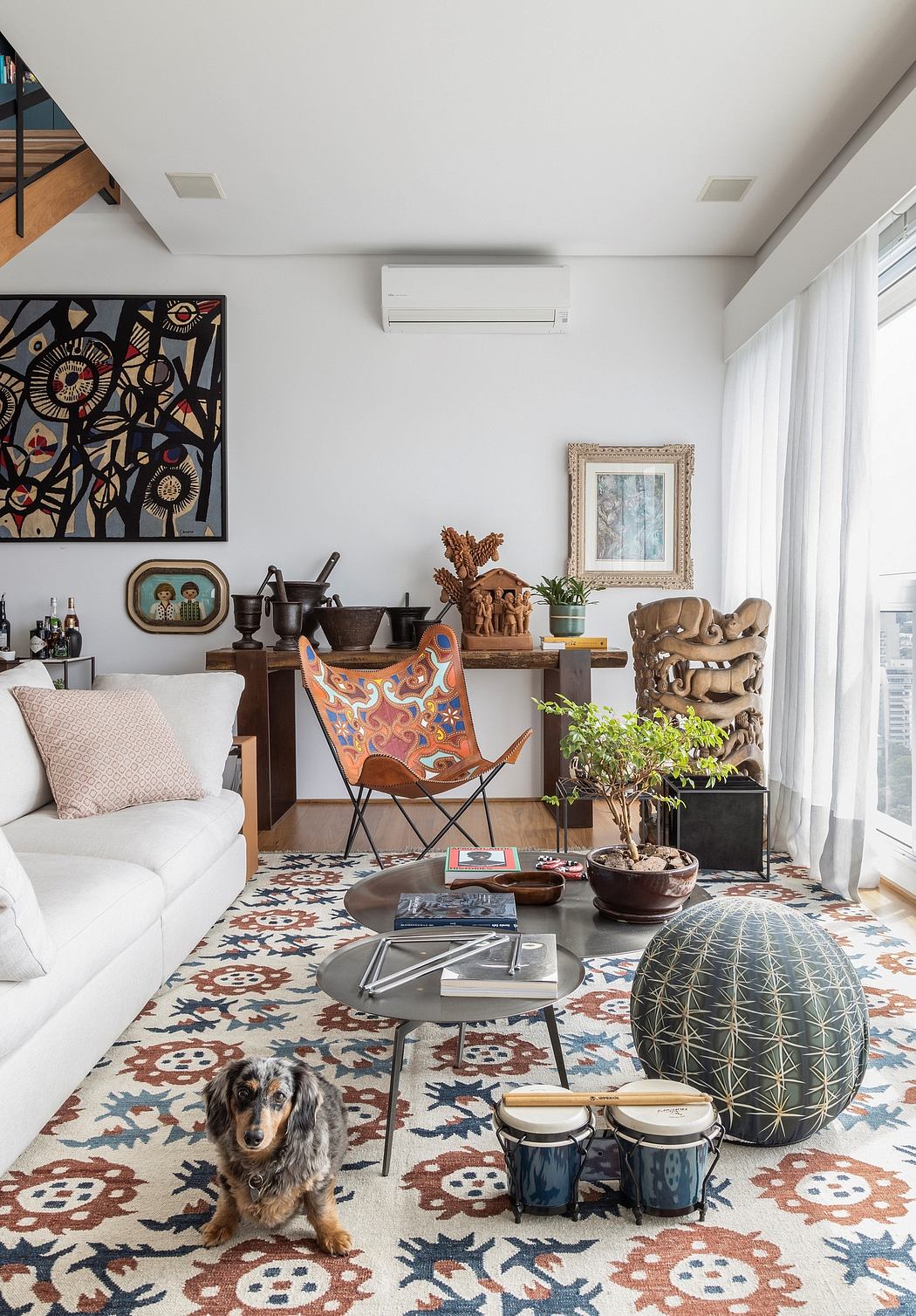 Eclectic living room with vibrant patterned rug, textured furniture, and potted plants.