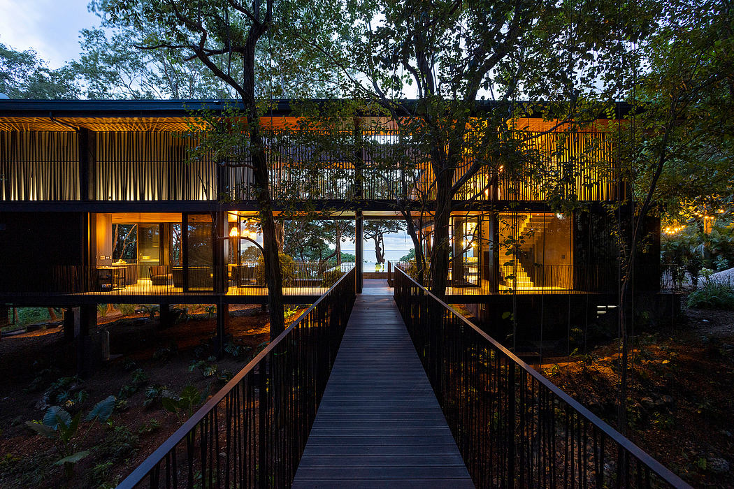 Elevated wooden walkway leads to a modern wooden lodge nestled in a lush, forested setting.