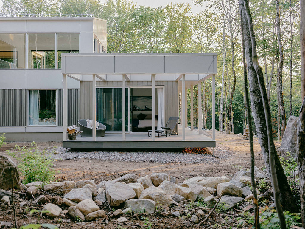 A contemporary glass-and-steel cabin surrounded by a lush forest landscape.