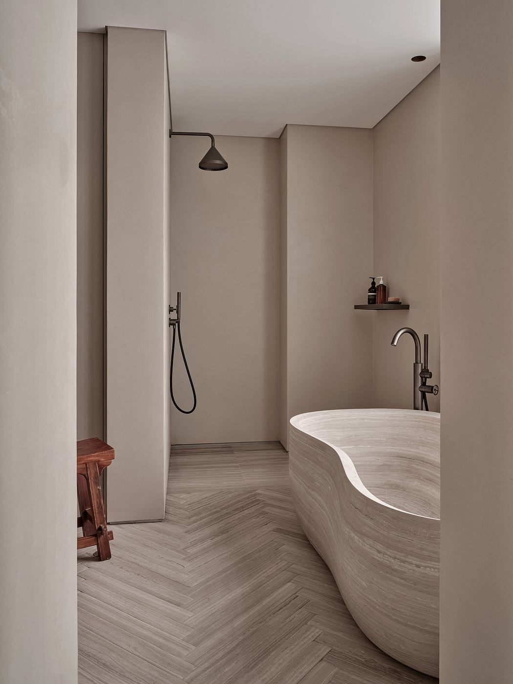 A modern bathroom with a curved white marble tub, black shower fixture, and herringbone floor tiles.