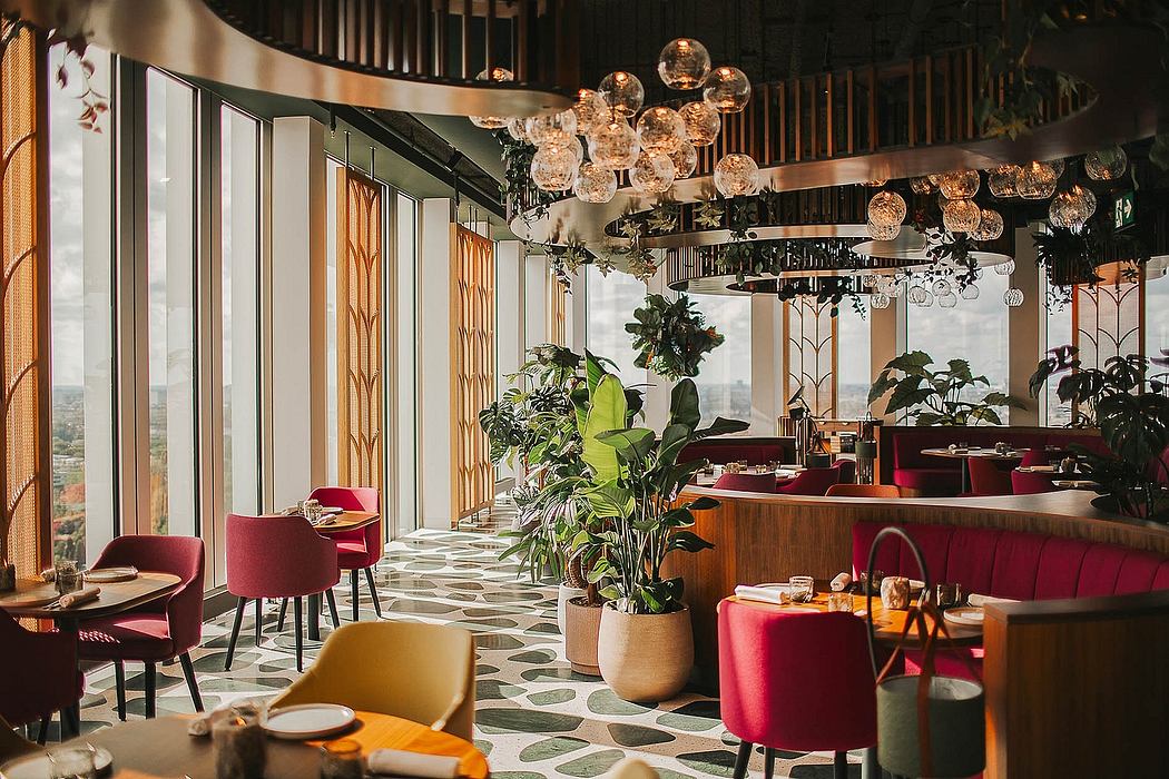 Vibrant, art-deco-inspired restaurant interior with pendant lighting, potted plants, and patterned flooring.
