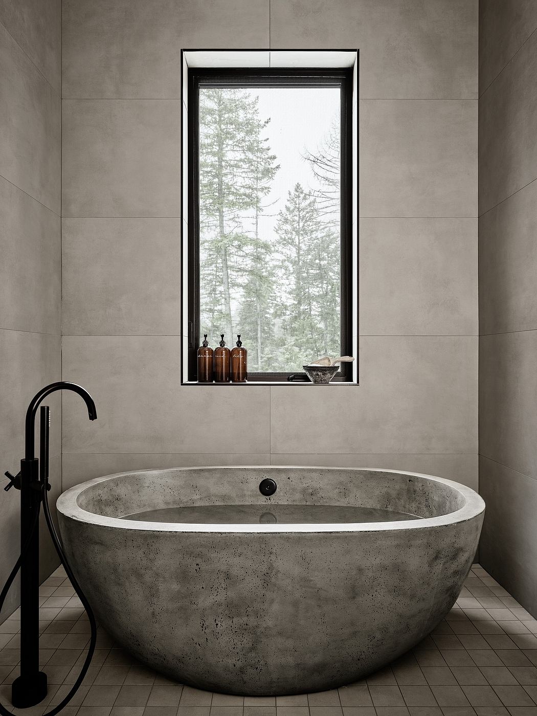 A minimalist bathroom with a concrete soaking tub, black faucet, and mountain views through the window.