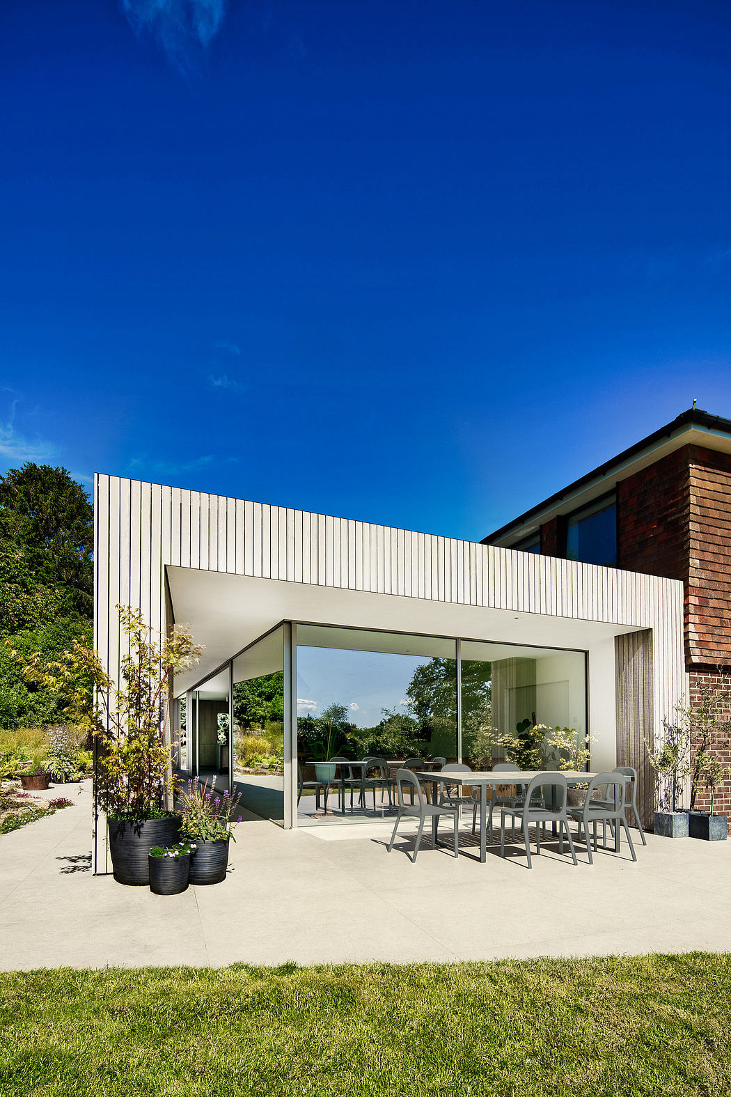 A modern home with a glass-enclosed patio, brick exterior, and lush landscaping.