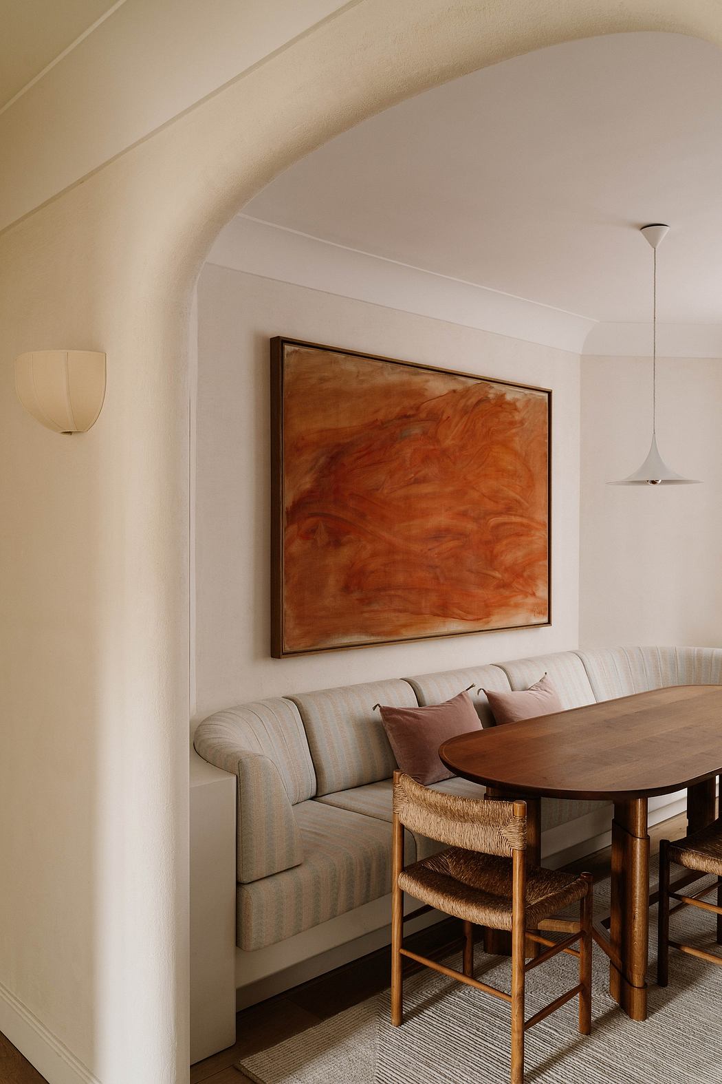 Cozy dining nook with curved ceiling, warm-toned artwork, and rustic wooden furniture.