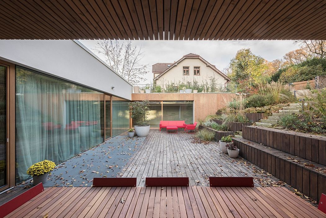 Wooden deck with glass walls, red seating, raised garden beds, and a traditional house.