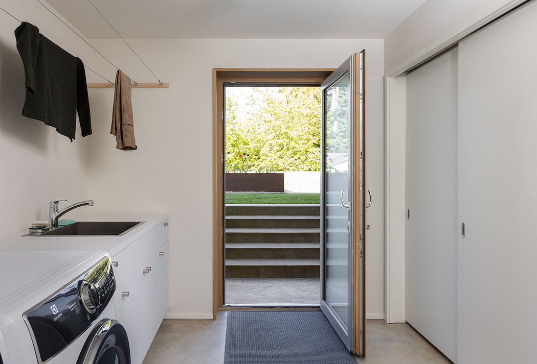 Spacious, modern laundry room with glass doors leading to outdoor steps and greenery.