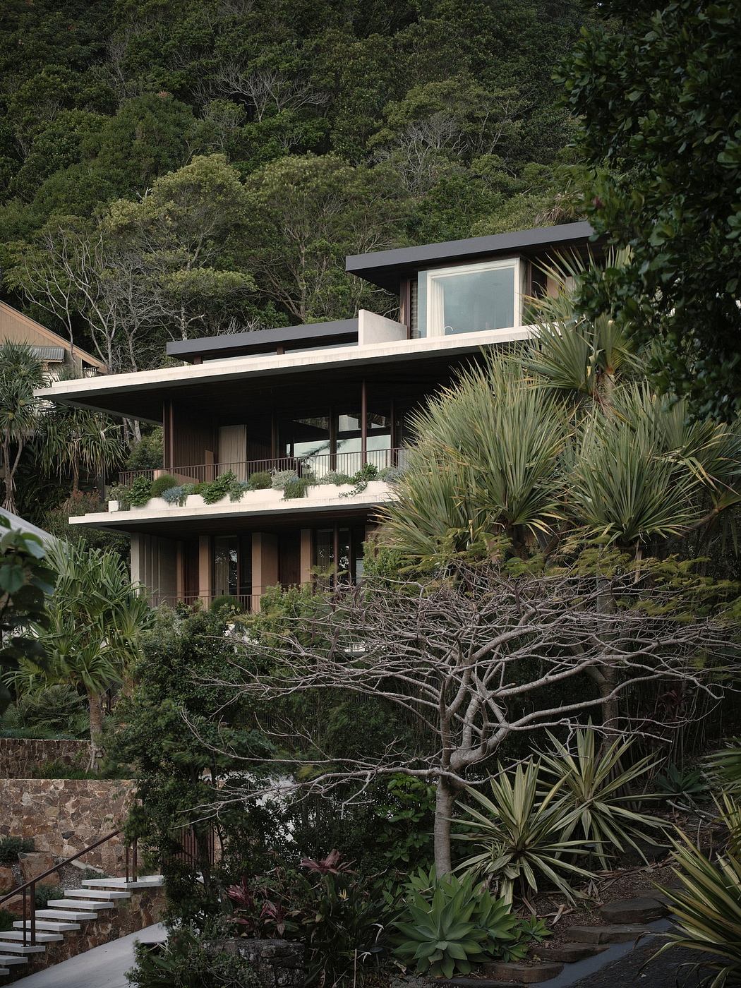 A modern, multi-level house nestled amidst lush, tropical vegetation and palm trees.