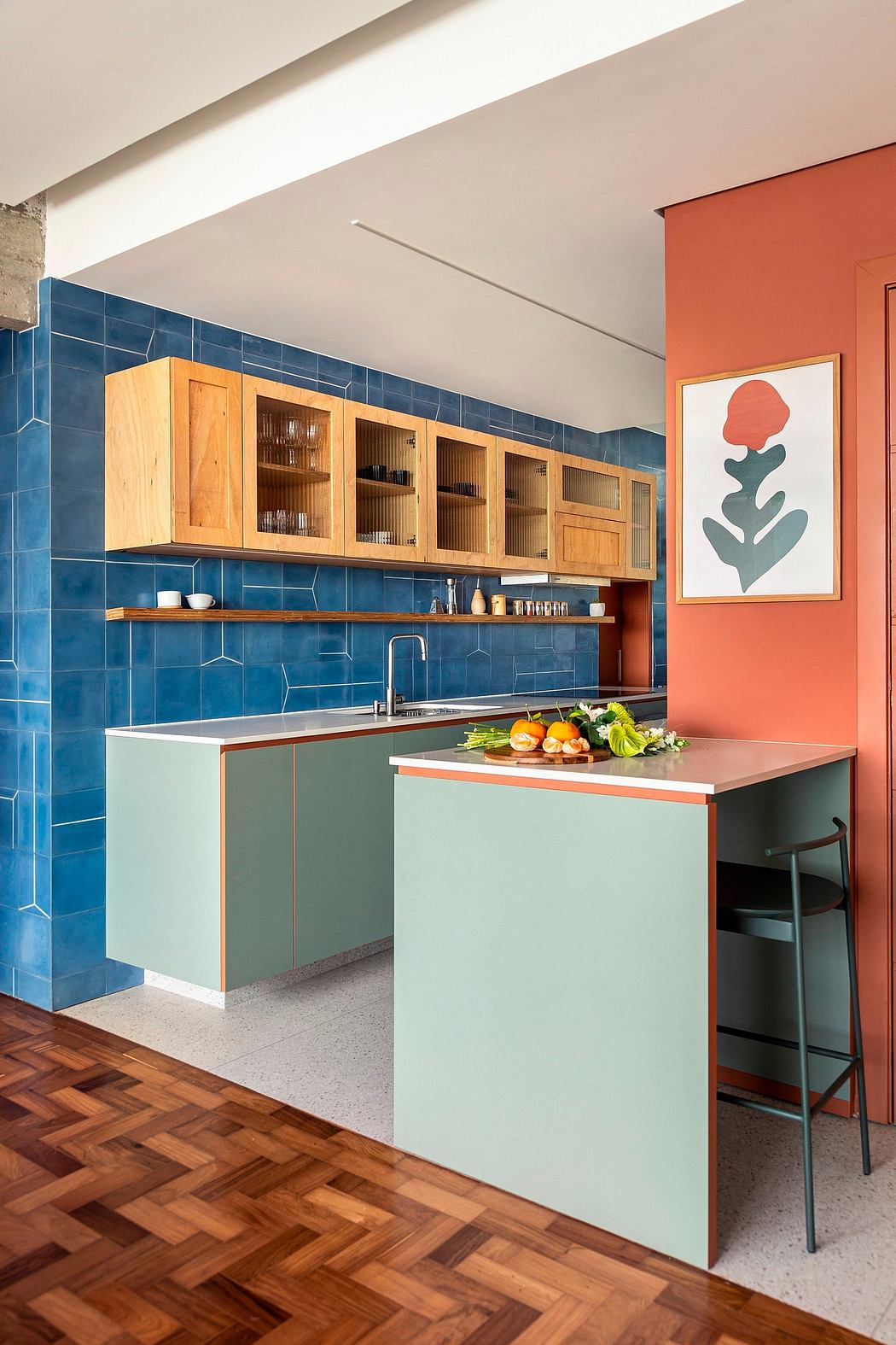 A modern kitchen with vibrant blue tiles, wood cabinets, and a minimalist green island.