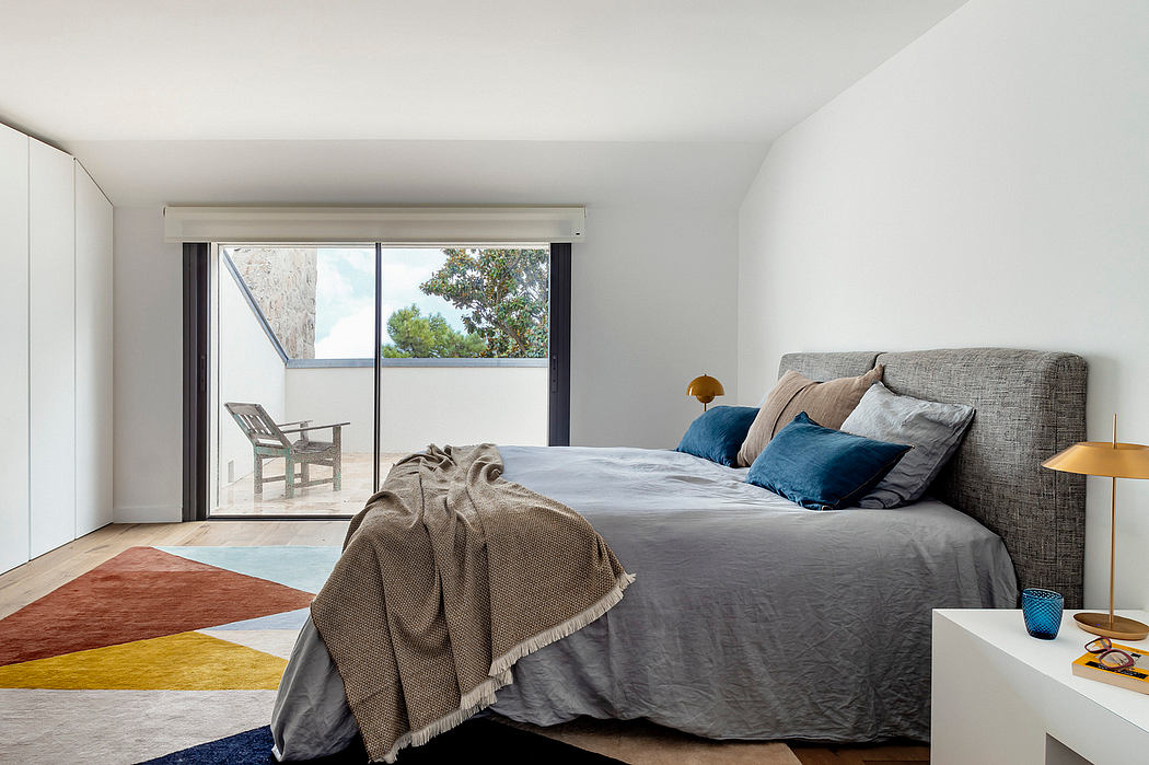 Minimalist bedroom with large sliding glass door, geometric rug, and neutral-toned furniture.