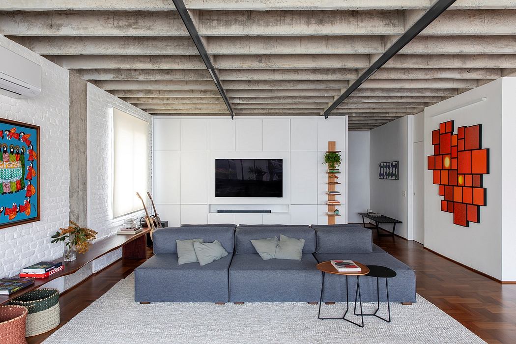 A modern living room with exposed wooden beams, gray sofa, and vibrant artwork.