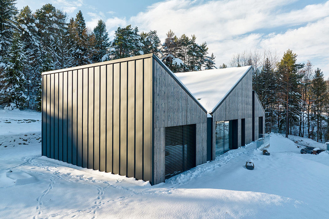 A modern, angular cabin nestled in a snowy, forested landscape.