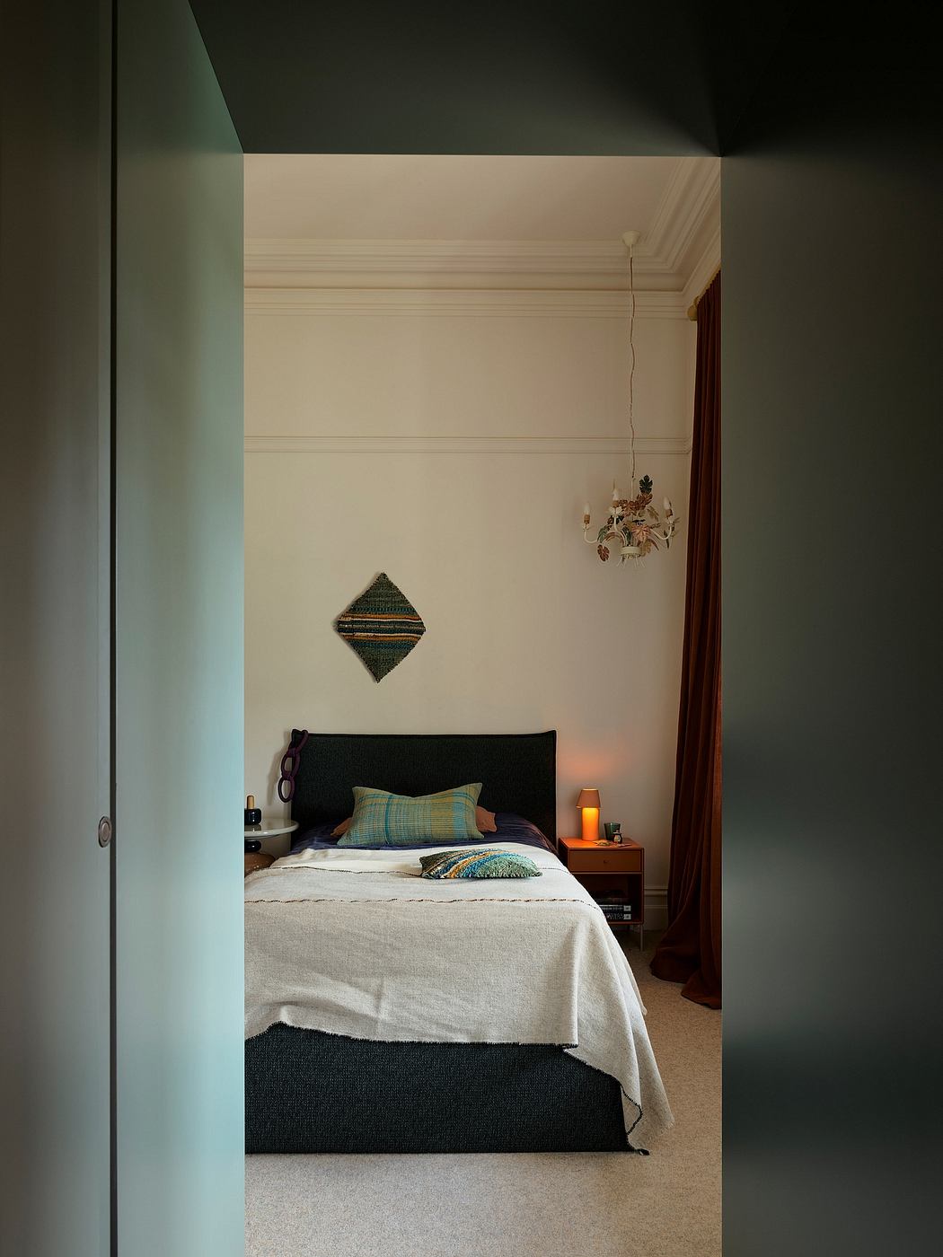 Cozy bedroom with dark headboard, textured pillows, and ornate wall sconce.