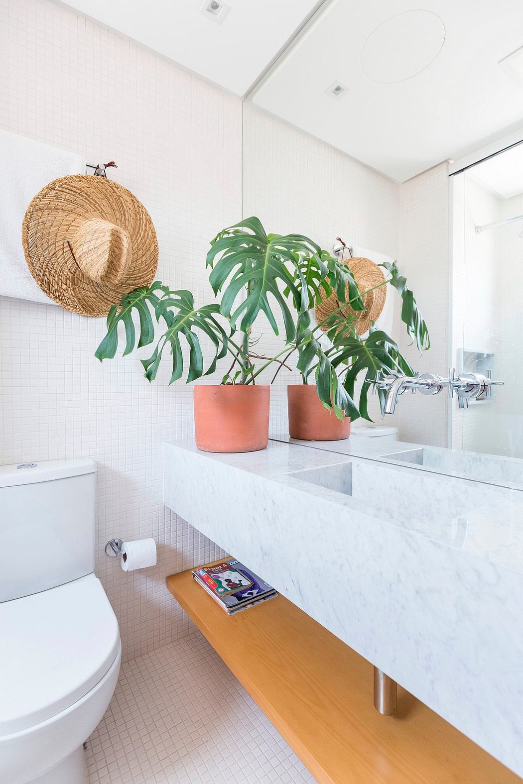Modern bathroom with white tile, marble vanity, and tropical plant decor.