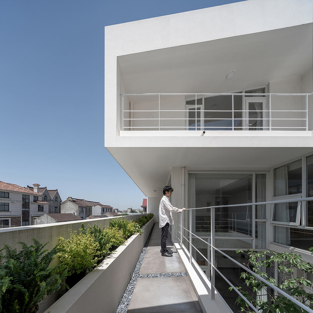 Minimalist residential exterior with balcony, vegetation, and a person observing the view.