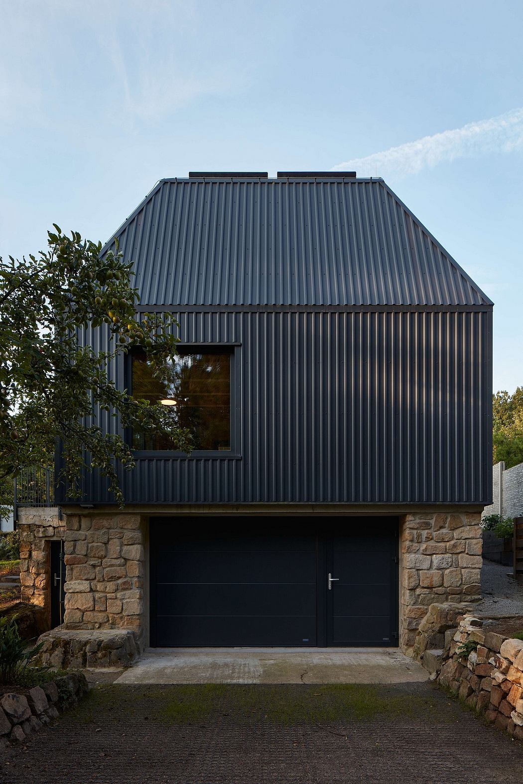 Modern building with slanted dark metal roof, stone walls, and garage door entrance.