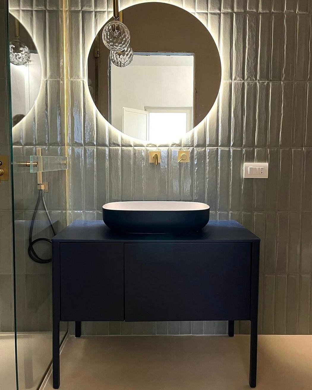 A contemporary bathroom vanity with black cabinets and a round mirror, complemented by glass tiles.