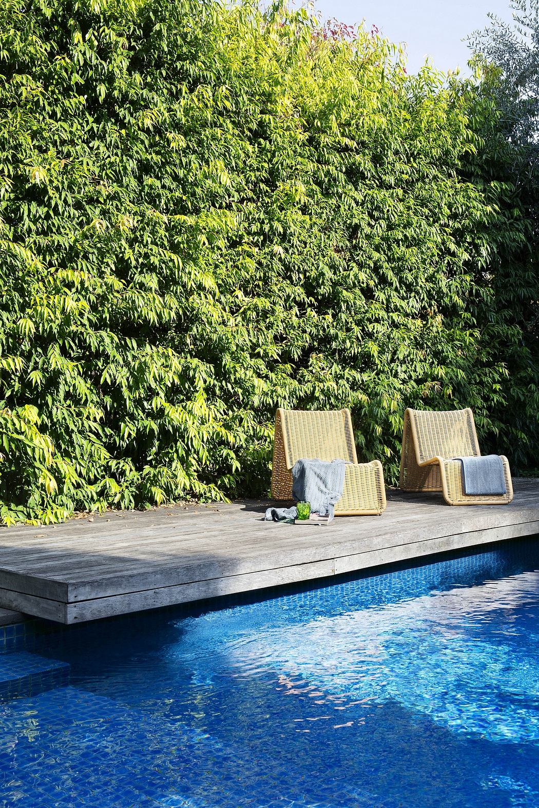 Tranquil pool surrounded by lush foliage and wicker patio furniture on a wooden deck.