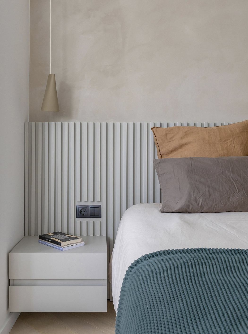 Minimalist bedroom with textured wall panels, neutral bedding, and a modern table lamp.