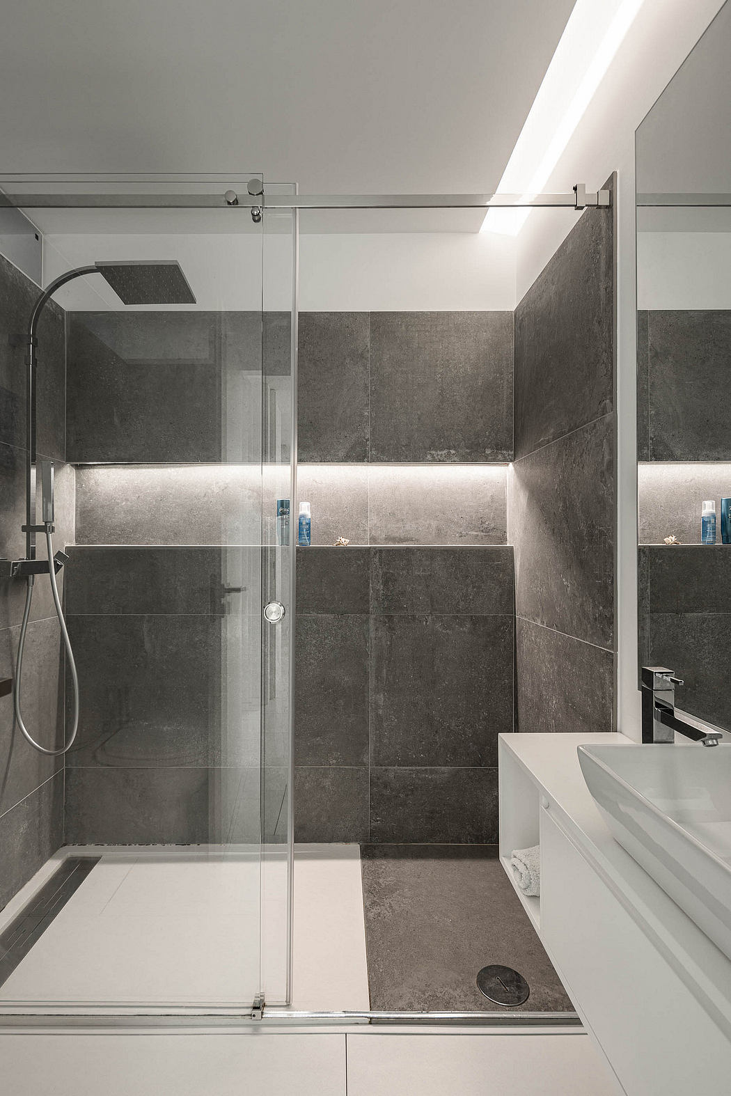 A modern bathroom with sleek glass shower enclosure and slate-tiled walls.