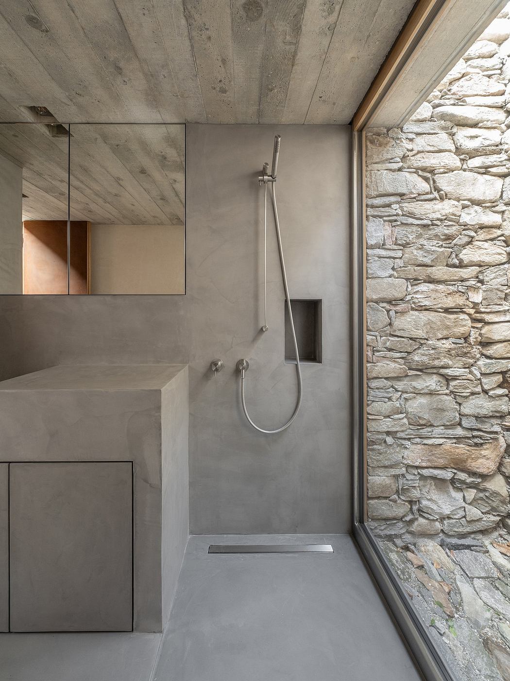 A modern, minimalist bathroom with a concrete vanity and stone wall feature.