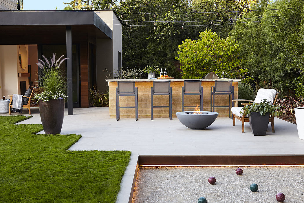 Sleek modern outdoor kitchen with a fire pit, planter boxes, and patio furniture on a grassy lawn.