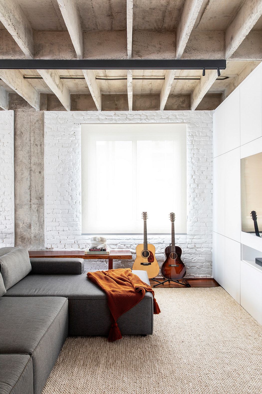 Minimalist loft-style interior with concrete ceiling beams, white brick walls, and acoustic guitars.