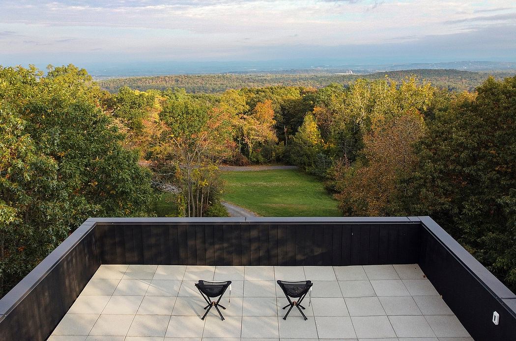 Elevated deck with black chairs overlooking lush, wooded landscape.