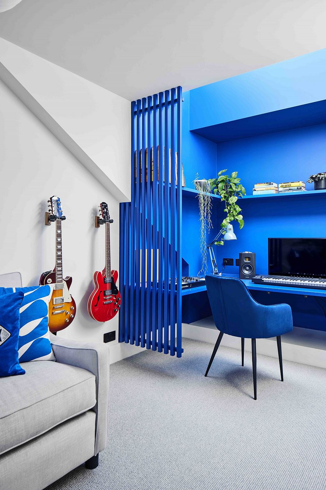 Vibrant blue accent wall, modern wood slat divider, electric guitars, and cozy furniture.