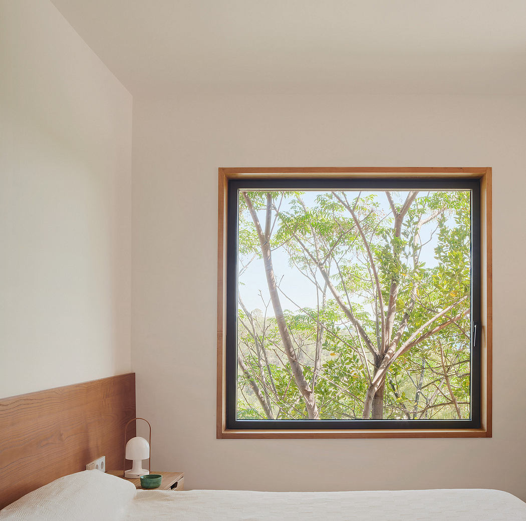Tranquil bedroom with wooden frame window overlooking lush green foliage.