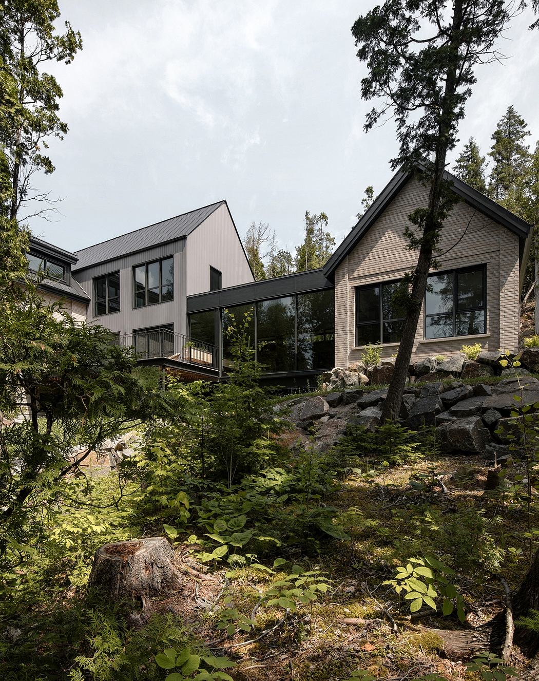 A modern, multilevel house nestled in a lush, forested landscape with large windows.
