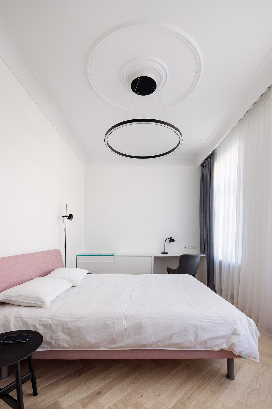 Clean, minimalist bedroom with circular ceiling light fixture, white bed, and built-in storage.