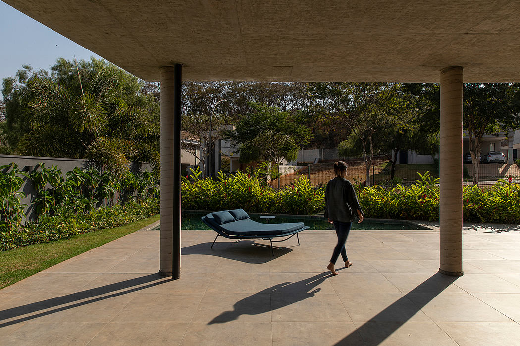Covered outdoor living area with concrete floor, lush landscaping, and modern furniture.