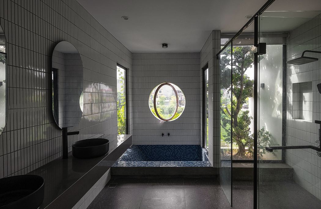 A modern bathroom with a circular window, black tiled surfaces, and large glass panels.
