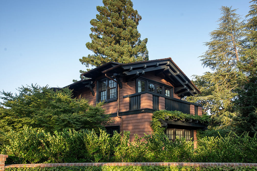 Rustic timber-framed house with large windows, sheltered porch, and lush surrounding vegetation.