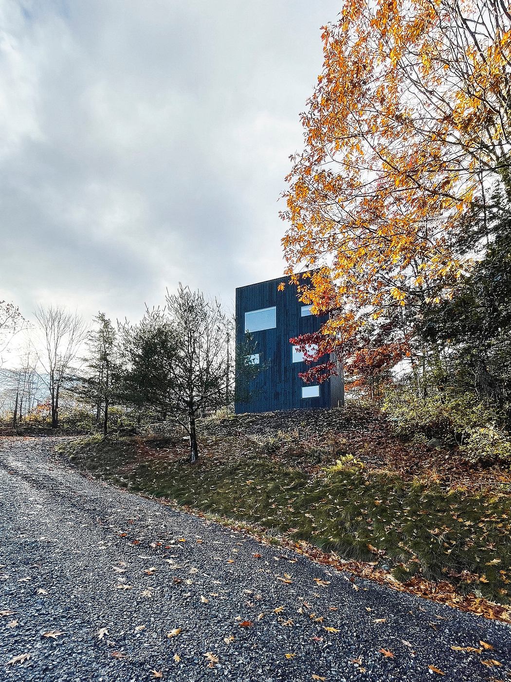 A dark, modern building nestled in a wooded, autumn-colored landscape.